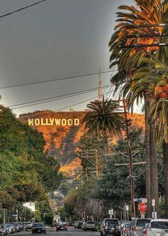 cars are parked on the street in front of hollywood sign and palm trees with mountains in the background