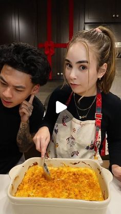 two people sitting at a table in front of a casserole dish