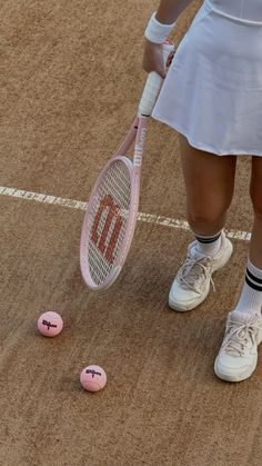 a woman holding a tennis racquet standing next to two pink balls on a court