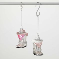 two glass snow boots hanging from hooks on a white wall, one with pink and silver trim