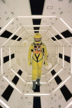 a man in yellow space suit standing in the middle of a white and black room