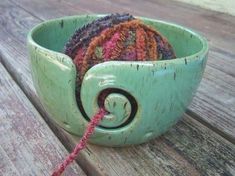 a yarn ball is in a green bowl on a wooden table with a red string