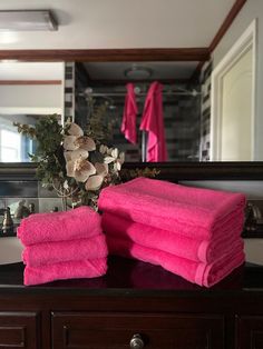 pink towels stacked on top of a wooden dresser in front of a mirror with flowers