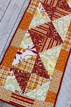 a quilted table runner with an orange and white pattern on the bottom, sitting on top of a wooden floor