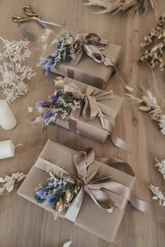 three wrapped presents sitting on top of a wooden table next to candles and dried flowers