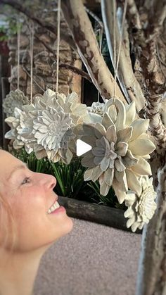 a woman smiling next to a tree with white flowers on it's branches and hanging decorations