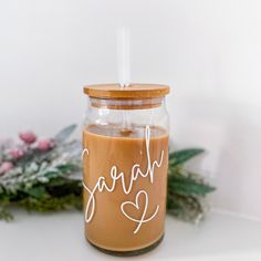 a jar filled with liquid sitting on top of a white table next to flowers and greenery