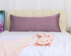 a white bed topped with a pink blanket next to a purple and green painting on the wall