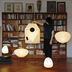 a person standing in front of a book shelf with several lamps on it and bookshelves behind them