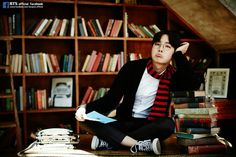 a young man sitting on the floor in front of bookshelves with his hands behind his head