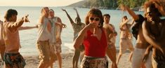 a group of people standing on top of a beach next to the ocean with drinks in their hands