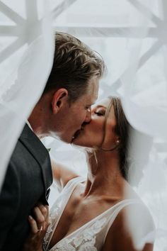 a bride and groom kissing each other in front of a white veiled window at their wedding