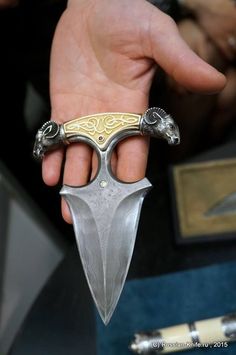 a hand holding a silver and gold colored knife in it's right hand, with two smaller blades sticking out of the blade