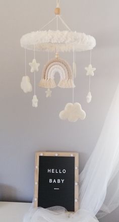 a baby crib with a chalkboard that says hello baby next to it is a cloud mobile