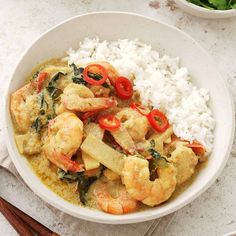 a white bowl filled with shrimp and rice next to chopsticks on a table