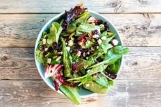 a green salad with nuts and cranberries in a blue bowl on a wooden table