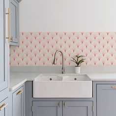 a kitchen with blue cabinets and pink wallpaper on the back splash, along with a white sink