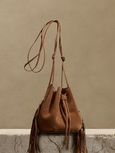 We updated our best-selling bucket bag, adding fringed leather accents and increasing storage space to accommodate even the largest phones.  Handcrafted in Italy of Italian suede.  Drawstring closure.  Adjustable shoulder strap.  Height: 7" (18cm) Diameter: 7" (18cm) Strap drop: 25" (38cm) Chic Travel Bucket Bag With Fringe, Suede Bucket Bag For Travel, Fall Bucket Bag For On-the-go, Fall On-the-go Bucket Bag, Leather Fringe Bucket Bag For Travel, Suede Bucket Bag With Removable Pouch For Travel, Chic Daily Use Bucket Bag With Tassels, Everyday Fringe Bucket Bag, Leather Bucket Bag With Tassels For Travel