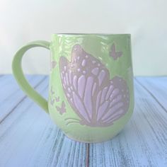 a green and pink coffee cup sitting on top of a white wooden table next to a wall