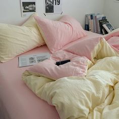 an unmade bed with pink sheets and pillows on it, next to bookshelves