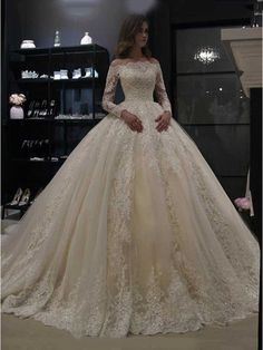 a woman standing in front of a display case wearing a wedding dress with long sleeves