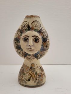 a ceramic vase with an artistic face on it's head, sitting on a white surface