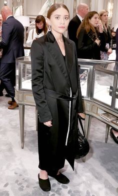 a woman standing in front of a glass display case at a fashion show with people looking on