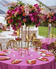 there is a table set up with purple and pink flowers in tall gold vases