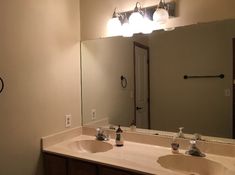 a bathroom with two sinks and a large mirror above the sink is lit by three lights