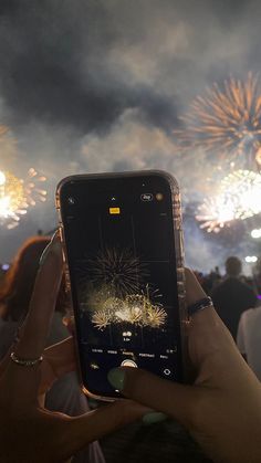 someone holding up their cell phone to take a photo with fireworks in the background