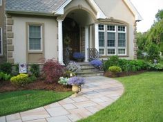 a house with landscaping in front of it and flowers on the side walk to the front door