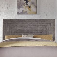 a bed with a wooden headboard in front of a white brick wall and painting on the wall