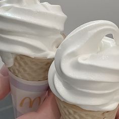 two ice cream cones with white frosting on top are being held by someone's hand