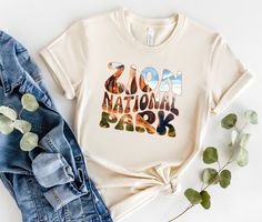 This T-shirt features the beautiful landscape of Zion National Park.  Take a piece of the great outdoors with you wherever you go with our National Parks themed t-shirt collection! Each shirt features a unique design inspired by one of America's iconic national parks, from the towering peaks of Yosemite to the otherworldly landscapes of Joshua Tree. These t-shirts are made from soft, comfortable cotton and come in a variety of sizes and colors to fit your style. They're perfect for wearing on yo Letter Print T-shirt For Outdoor In Spring, Letter Print T-shirt For Outdoor Spring Activities, Graphic Tee For Outdoor Activities In Spring, Spring Letter Print Top For Outdoor Activities, Park Ranger Aesthetic, Ranger Aesthetic, Girl Camping, Camping Clothes, National Park Shirt