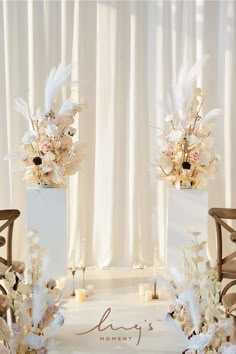 two tall vases with flowers and feathers are sitting on a table in front of a white curtain