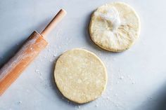 two uncooked pita breads next to a rolling pin on a counter