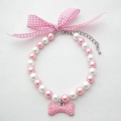 a bracelet with pink and white pearls and a bow charm on it, sitting on top of