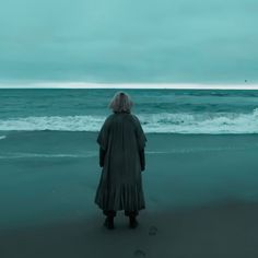 a woman standing on top of a sandy beach next to the ocean under a cloudy sky