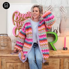 a woman sitting on top of a wooden table wearing a colorful knitted cardigan