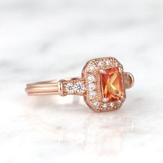 Gorgeous Vintage Inspired Orange Sapphire Ring ►Made of solid sterling silver with the 14k rose gold finish (925) ►Accented With Simulated Diamonds (CZ) ►Average band width: 2.3 mm ►Halo size: 9.9mm x 8.3mm Center Stone: Sapphire Color: Orange Measurements: 4.0 x 6.0 mm Carat Weight: 0.7 ct. (approx.) Gemstone creation: 100% Natural Hardness: 9-9.5 (Mohs scale) ►Please be aware that plated jewelry can wear off over time, if this is a concern we would suggest going with the sterling silver or sol Classic 14k Rose Gold Emerald Cut Ring, Classic Rose Gold Cluster Ring With Halo Design, Classic Rose Gold Cluster Ring With Halo, Classic Rose Gold Birthstone Ring For Formal Occasions, Classic Rose Gold Halo Cluster Ring, Vintage Rose Gold Rings With Accent Stones, Classic Rose Gold Cluster Ring With Center Stone, Classic Rose Gold Rings With Accent Stones, Classic Rose Gold Birthstone Ring For Anniversary