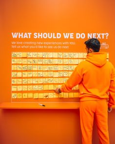 a man in an orange hoodie writing on a board with notes attached to it