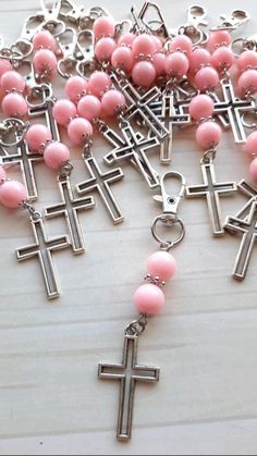 pink beads and silver cross charms on a white table with a chain hanging from it