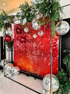 christmas decorations on display in front of a red wall with silver balls and greenery