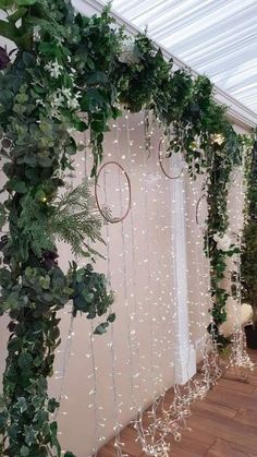 an indoor wedding ceremony with greenery and white lights hanging from the ceiling, along with sheer curtains