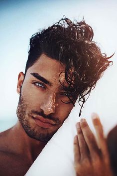 a man with wet hair and blue eyes holding his hand up in front of him