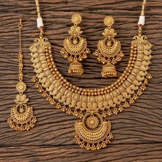 a gold necklace and earring set on a wooden surface, with beads hanging from it