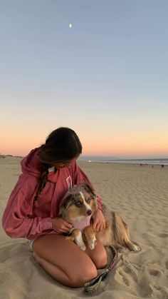 a woman sitting on top of a sandy beach holding a dog