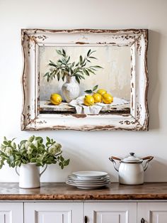 a painting hanging on the wall above a buffet with lemons and white dishes in front of it