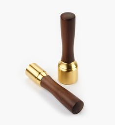 two brass and wood pepper grinders on a white background, one with a wooden handle