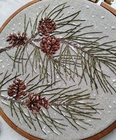 a close up of a embroidery on a piece of cloth with pine cones and needles